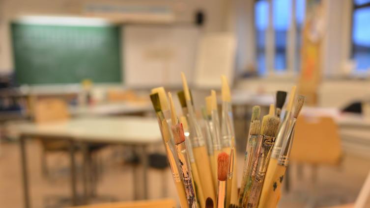 Bilde av malepensler i forgrunn og klasserom diffus i bakgrunn - Klikk for stort bilde